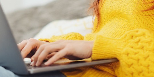 Kvinna med gul tröja med en dator i knät.