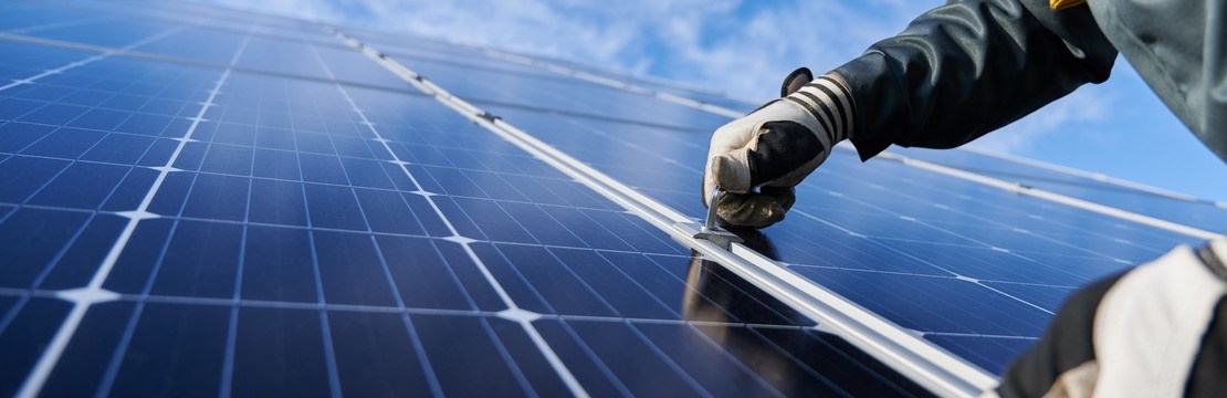 Närbild på händer med skyddshandskar som fäster en solpanel.