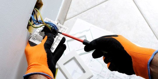 Närbild på händer med handskar som installerar ett vägguttag i en bostad.