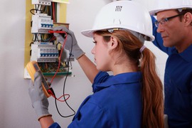 Kvinnlig och manlig elektriker vid en elcentral.