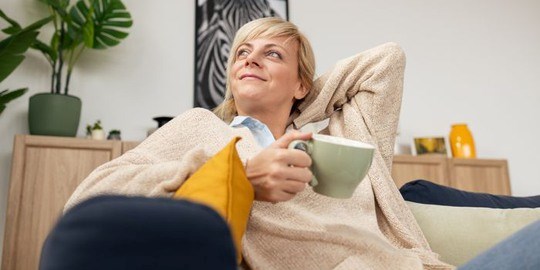 En kvinna i en soffa med kaffekopp i handen.