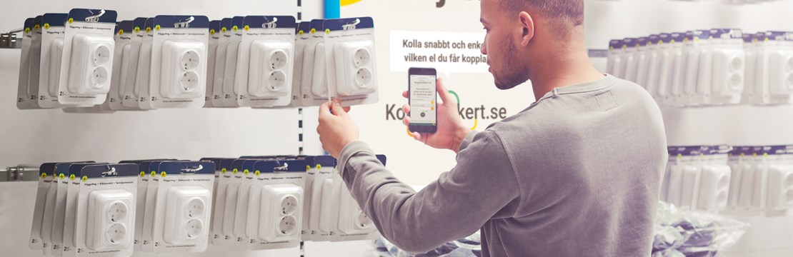 Manlig kund i butik framför kontaktuttag tittar på sin mobiltelefon.