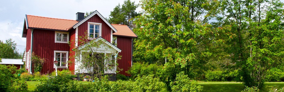 Röd villa, gräsmatta och träd sommartid.