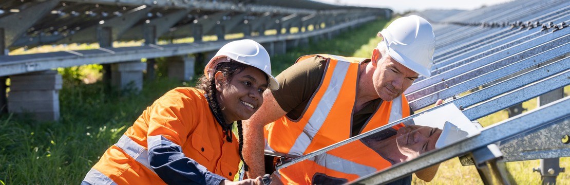 Man och kvinna i hjälm och skyddskläder hjälps åt att installera en solpanel i en solcellspark.