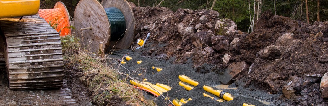 grävmaskinshjul till vänster och ytligt nedgrävda kablar till höger samt en kabeltrumma i centrum