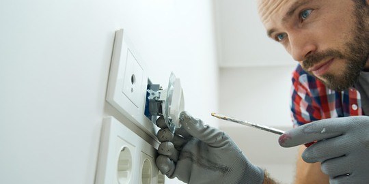 Ung man bär skyddshandskar och ser fokuserad ut när han installerar ett eluttag.