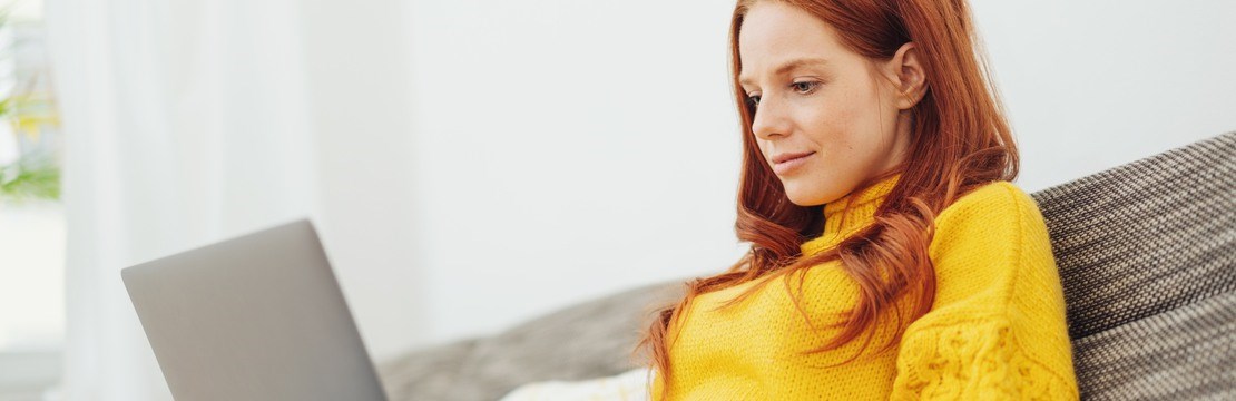 Kvinna med gul tröja med en dator i knät.