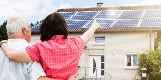 Äldre par framför hus med solpaneler.
