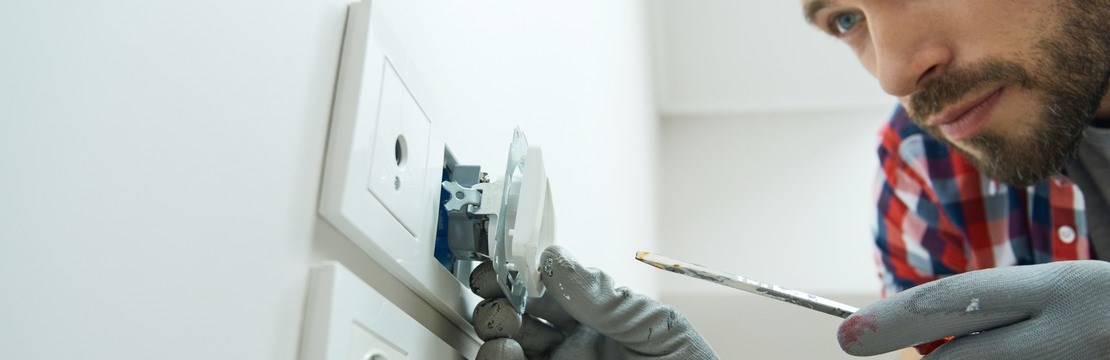 Ung man bär skyddshandskar och ser fokuserad ut när han installerar ett eluttag.