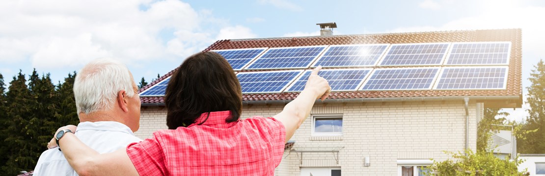 Äldre par framför hus med solpaneler på hustak.