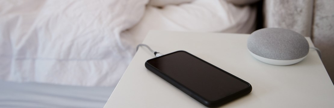 Mobiltelefon laddas på nattduksbord.