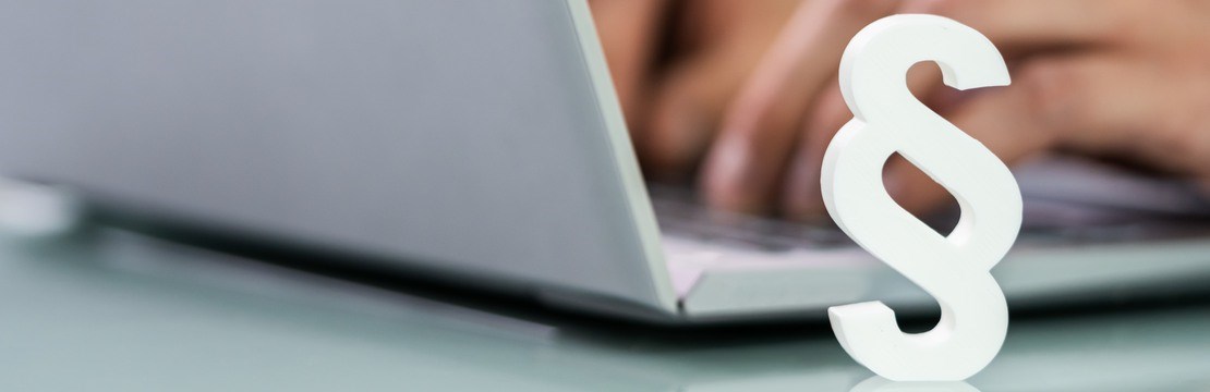 Ett vitt paragraftecken står intill en öppnad laptop, där en person sitter och skriver vid tangentbordet.