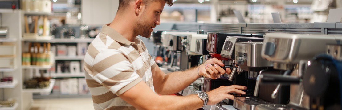 Manlig kund vid hylla med kaffemaskiner i en affär.