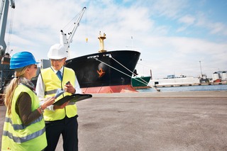 Tullarbetare i hamn med skepp i bakgrunden.