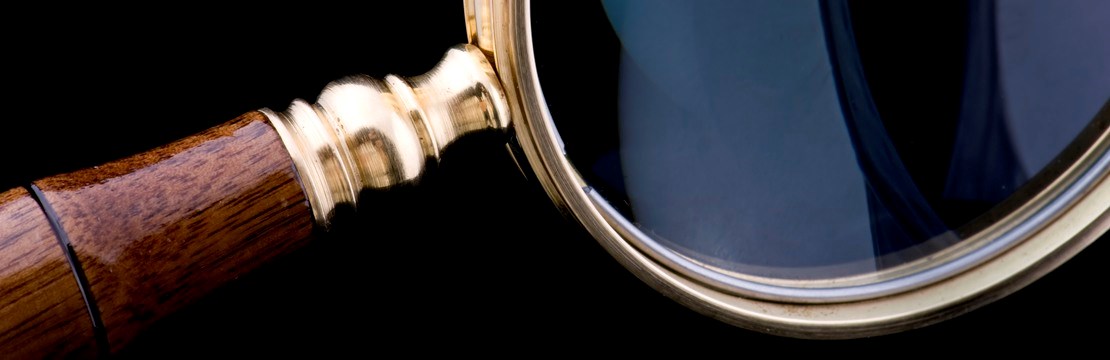  Närbild på ett förstoringsglas med svart bakgrund. Ett paragraftecken står på ett ljust trägolv och lutar mot en blå vägg.