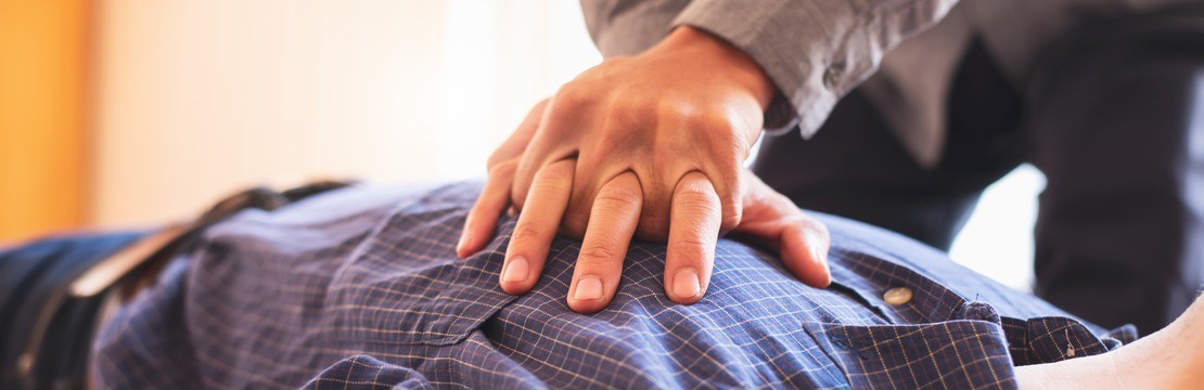 Händer utför akut hjärt-lungräddning på man med skjorta.