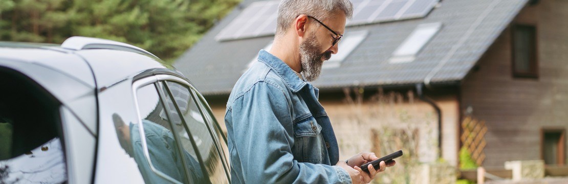 Portrait of a man charging his electric car in front of his house, plugging the charger into the charging port. The man is unplugging the charger from the fully charged car before going to the office.