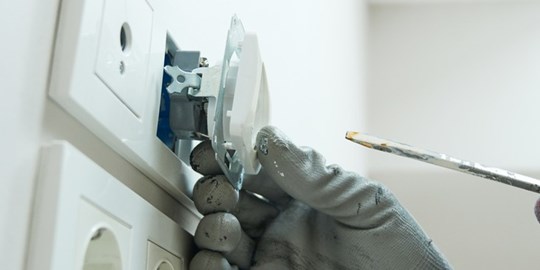 Ung man bär skyddshandskar och ser fokuserad ut när han installerar ett eluttag.