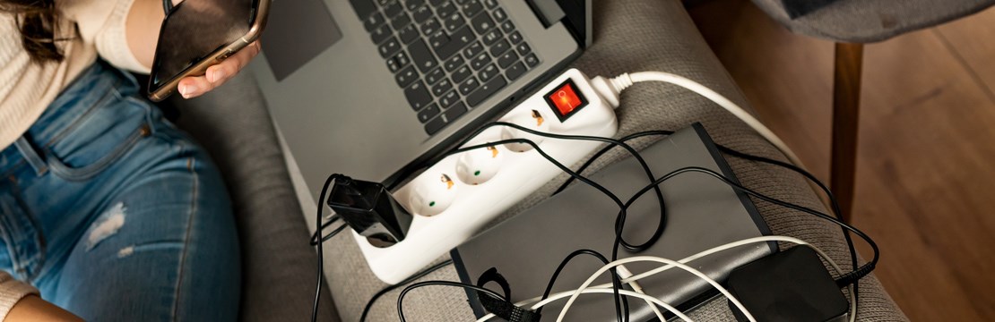 Tjej sitter i soffa med mobiltelefon och en massa laddare i ett grenuttag.
