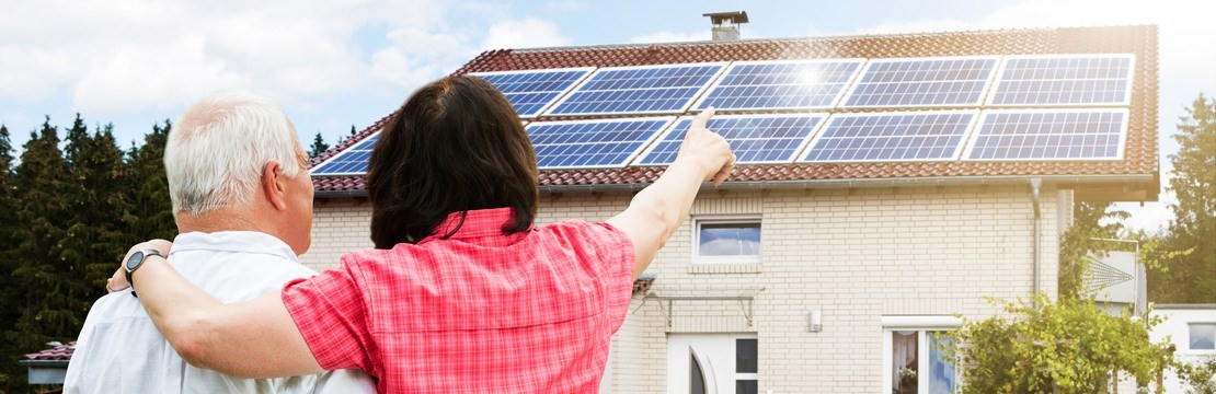 Äldre par framför hus med solpaneler.