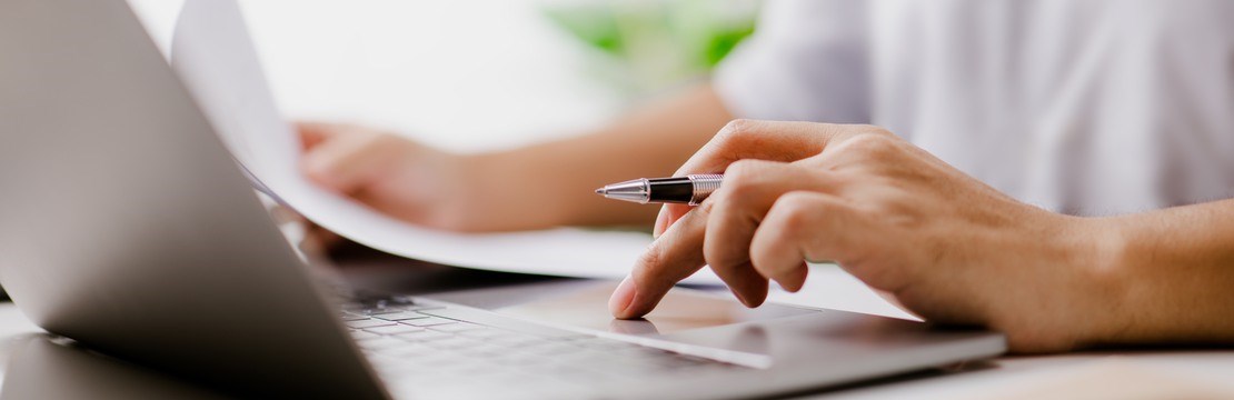 Hand skriver på laptop och håller samtidigt ett papper i den andra handen. 