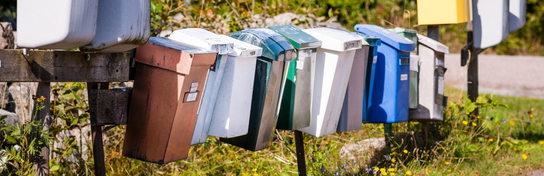 Flera brevlådor på rad vid landsväg sommartid.