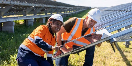 Man och kvinna i hjälm och skyddskläder hjälps åt att installera en solpanel i en solcellspark.