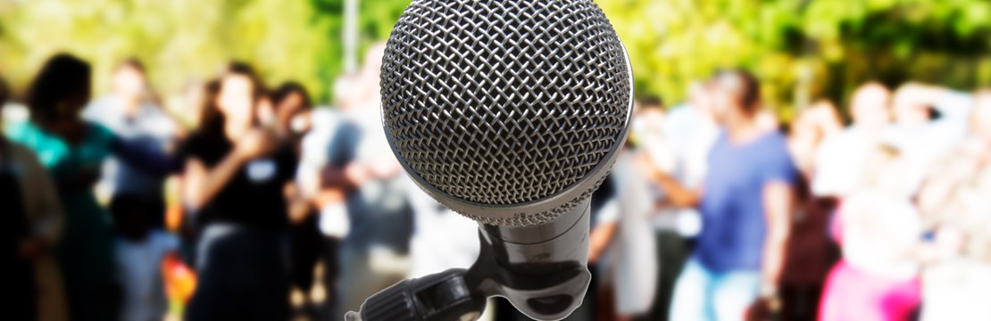 En mikrofon i närbild framför publik utomhus.