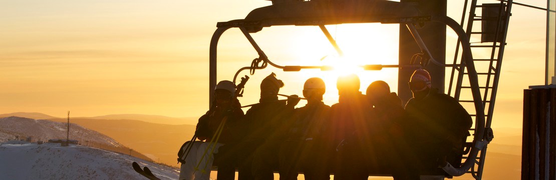 Ett gäng skidåkare i en sittlift med solnedgång i bakgrunden.