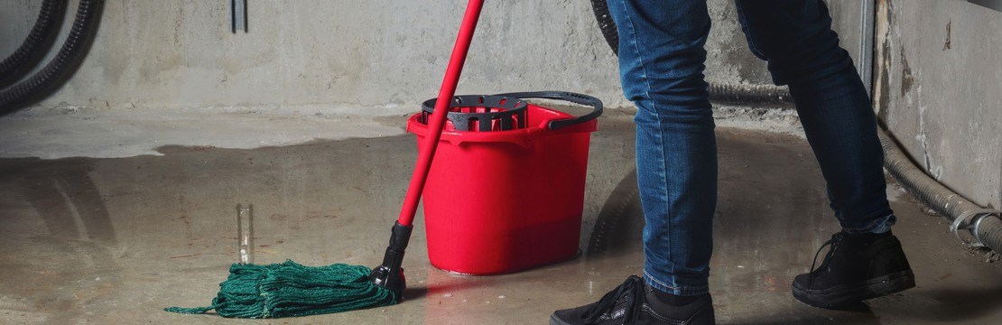 Person som moppar vatten från golv i en källare.