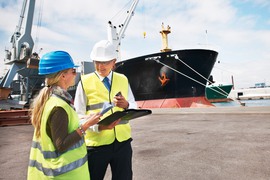 Tullarbetare i hamn med skepp i bakgrunden.