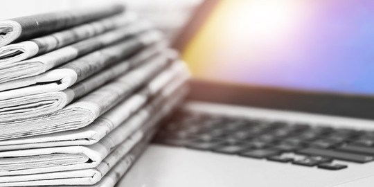 En stapel tidningar och en laptop.