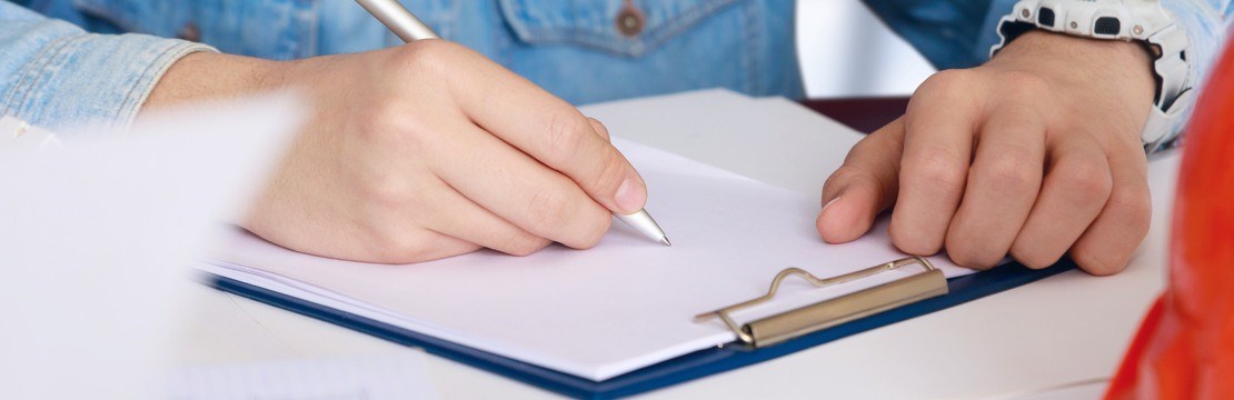 Man med skjorta sitter vid ett bord och skriver anteckningar med en skyddshjälm vid sidan om sig. 