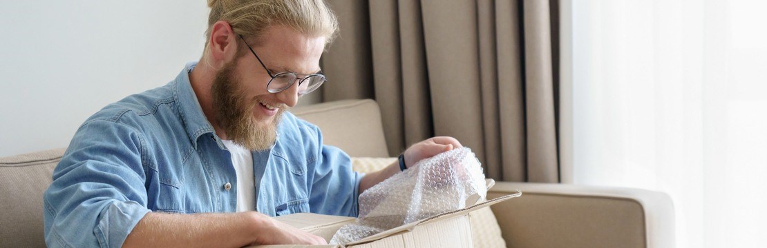 Glad man öppnar en kartong med bubbelplast i soffan.