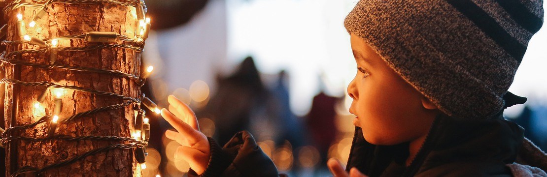 Ett barn rör vid en ljusslinga på ett träd.