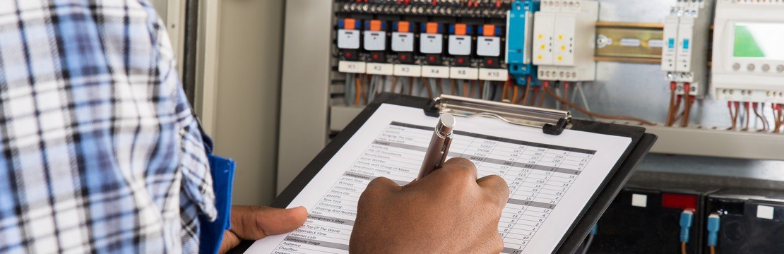 En elinstallatör framför en elcentral med checklista.