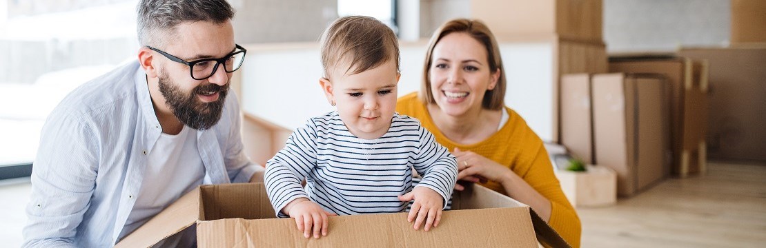 Litet barn sitter i flyttkartong med föräldrarna på varsin sida. 