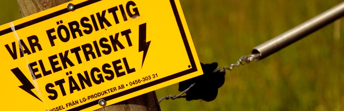 Gul skylt med svart text som lyder var försiktig, elektriskt stängsel.