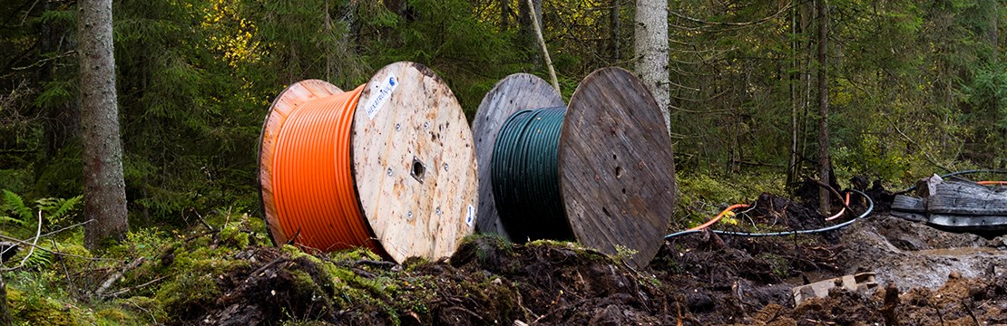 Två kabeltrummor på uppgrävd lerig mark intill skogsbryn.