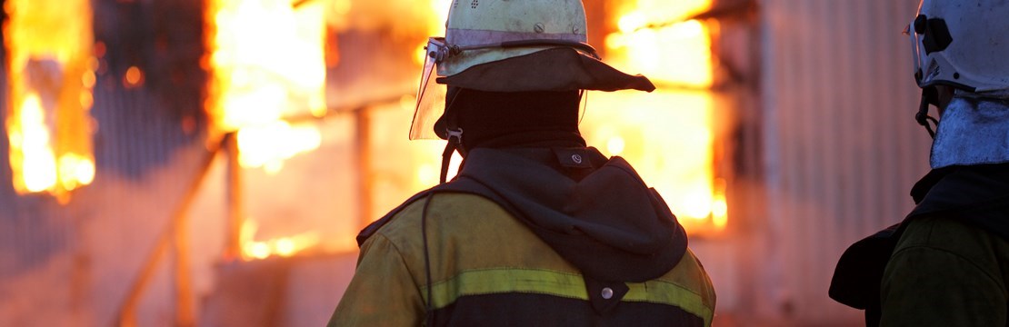 Profilen av två brandmän med brinnande hus i bakgrunden.