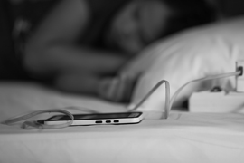 en mobil laddas i sängen med sovande kvinna bredvid