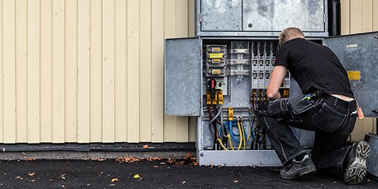 Elektriker står på knä framför öppet elskåp