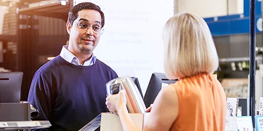 Två personer interagerar över en butiksdisk om en elektrisk produkt.