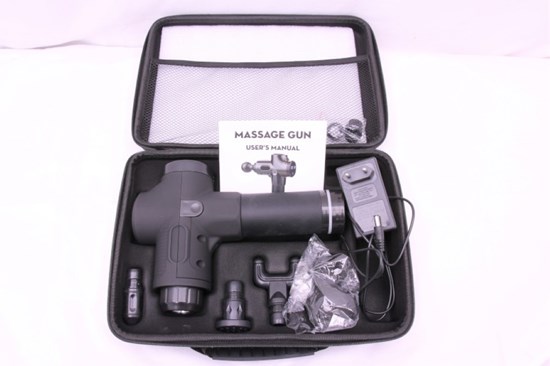 Svart massagapistol med vit manual och svart adapter liggandes i en svart väska