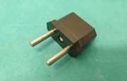 Svart adapter med silverfärgade stift. Turkos bakgrund
