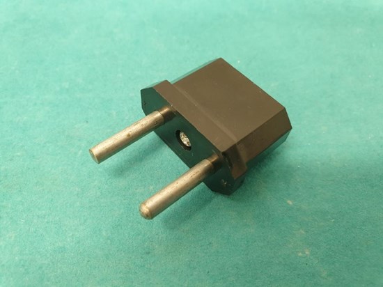 Svart adapter med silverfärgade stift. Turkos bakgrund