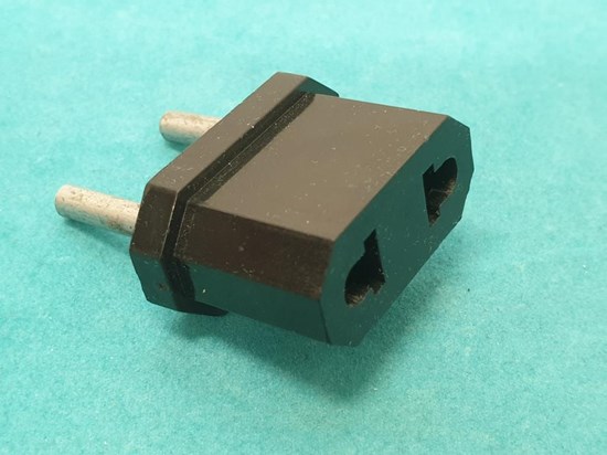 Svart adapter med silverfärgade stift. Turkos bakgrund. Sedd bakifrån