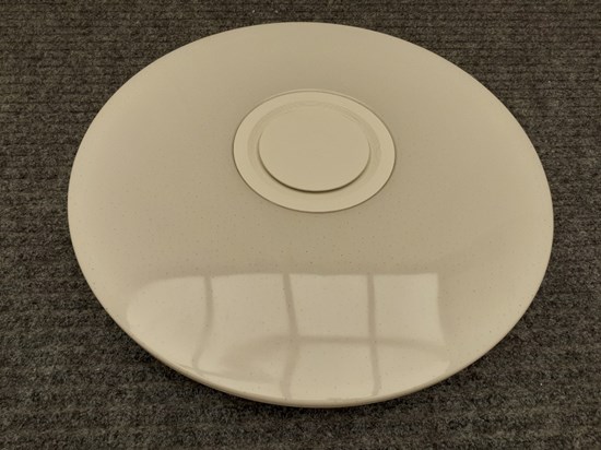 Rund vit lampa gjord av plast. Mindre rund ring i mitten av lampan. 