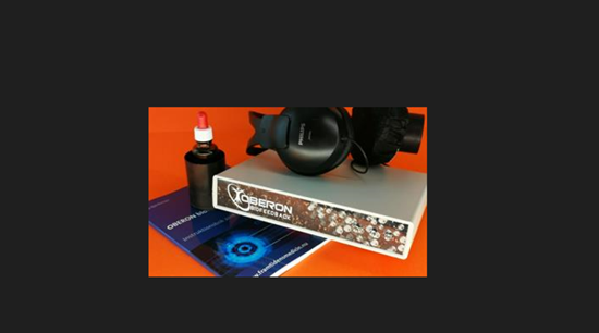 Vit box som ligger på en blå bok mot orange och svart bakgrund. På boxen ligger ett par svarta hörlurar med en svart flaska intill.